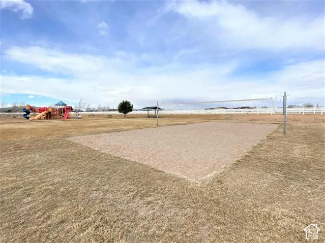 Expansive outdoor grounds featuring a sand volleyball court, integrated playground equipment, covered pavilion, and perimeter white fencing