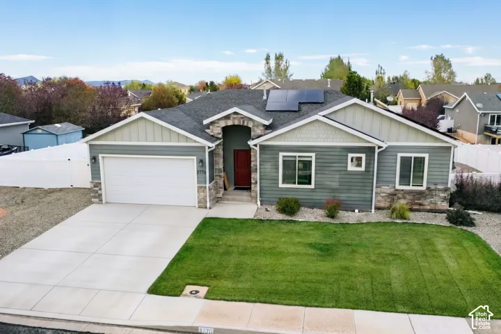 Single-story residence featuring composite siding, stone veneer accents, a concrete driveway, an attached two-car garage, and installed rooftop solar panels