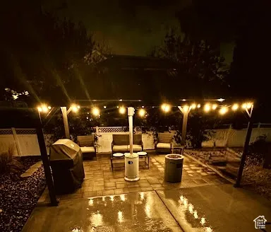 Backyard patio featuring a hardscaped paver surface, a permanent metal-frame pergola, integrated string lighting, and white lattice-top privacy fencing