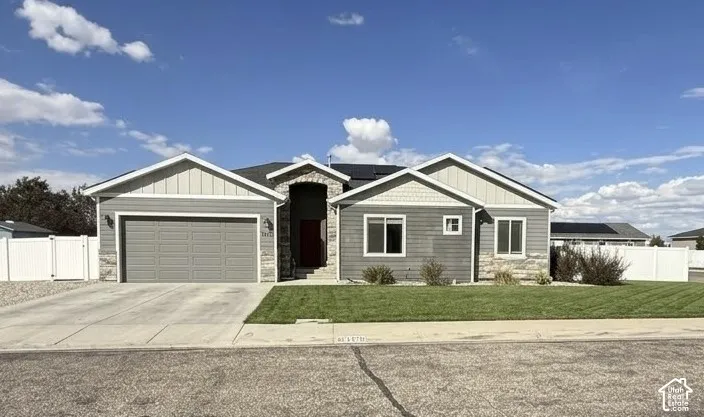 Single-story exterior featuring a mix of horizontal siding and stone veneer, a covered entryway with an arched stone surround, an attached two-car garage, roof-mounted solar panels, and a fenced yard