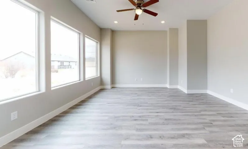 Spacious room featuring wood-finish flooring, recessed lighting, a ceiling fan, and large windows providing natural light