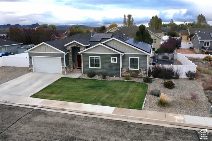 Single-level residence featuring a stone-accented facade, lap siding, solar panels, a two-car garage, and a fenced yard