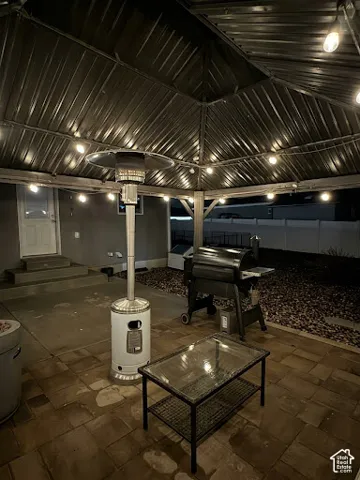 Covered patio area featuring a metal roof structure, string lighting, paved flooring, and concrete steps leading to the main structure