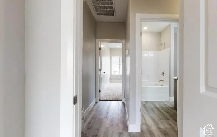 Hallway featuring wood-finish flooring, recessed lighting, and a bathroom with a white tub and shower surround