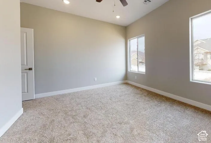 Neutral-toned room featuring vaulted ceilings, plush carpeting, dual-pane windows, and a central ceiling fan