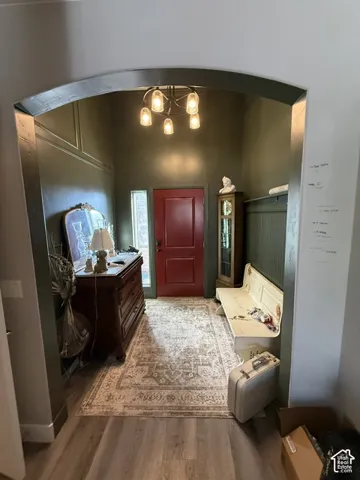 Foyer featuring an arched entryway, wood-finish flooring, beadboard wall paneling, and a multi-bulb overhead light fixture