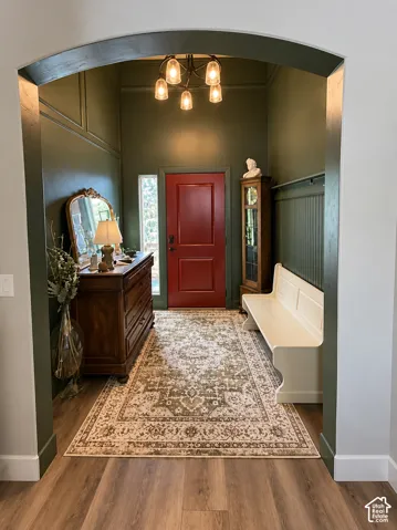 Entryway featuring a prominent arched transition, wood-finish flooring, wainscoting detail, and a five-light chandelier