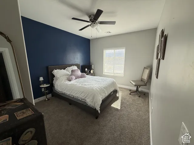 Room featuring a navy blue accent wall, neutral carpeting, ceiling fan with light fixture, and windows equipped with horizontal blinds