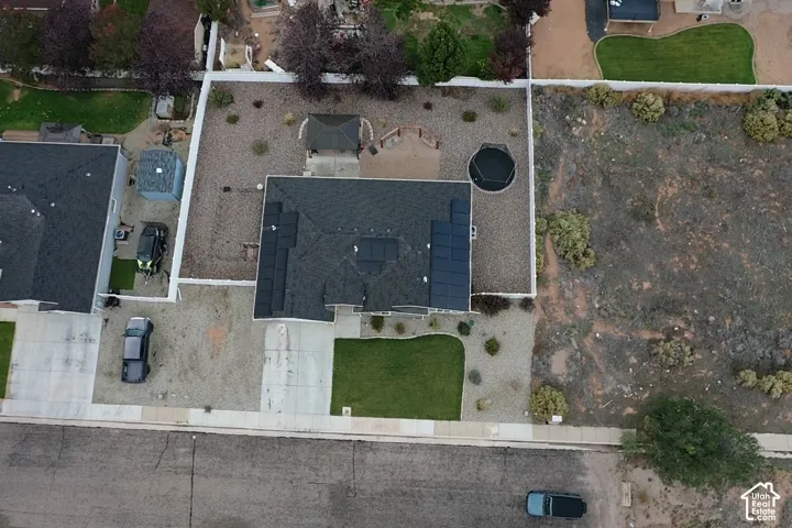 Aerial perspective of a property featuring roof-mounted solar panels, a paved driveway, a manicured front lawn, a fully fenced backyard with a gazebo, and xeriscape landscaping