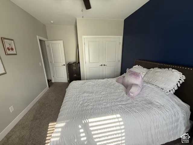 Bedroom featuring a deep blue accent wall, neutral carpeting, double-door closet, and ceiling fan