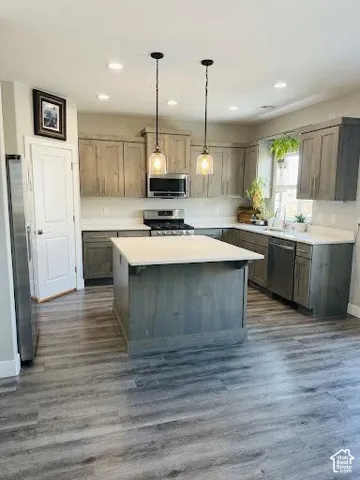 Kitchen featuring a center island, wood-finish cabinetry, quartz countertops, stainless steel appliances, and wood-finish flooring