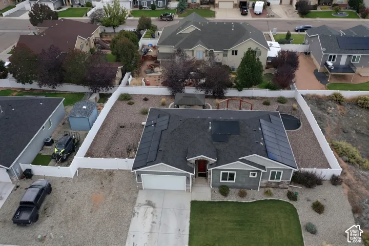 Aerial perspective of a residence featuring solar panel arrays, a multi-car garage, fenced backyard, stone and siding exterior cladding, and hardscaped landscaping
