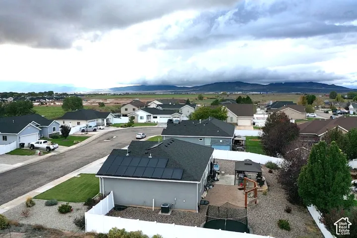 Aerial perspective of residential property featuring roof-mounted solar panels, fenced yard with stone ground cover, and mountain range backdrop