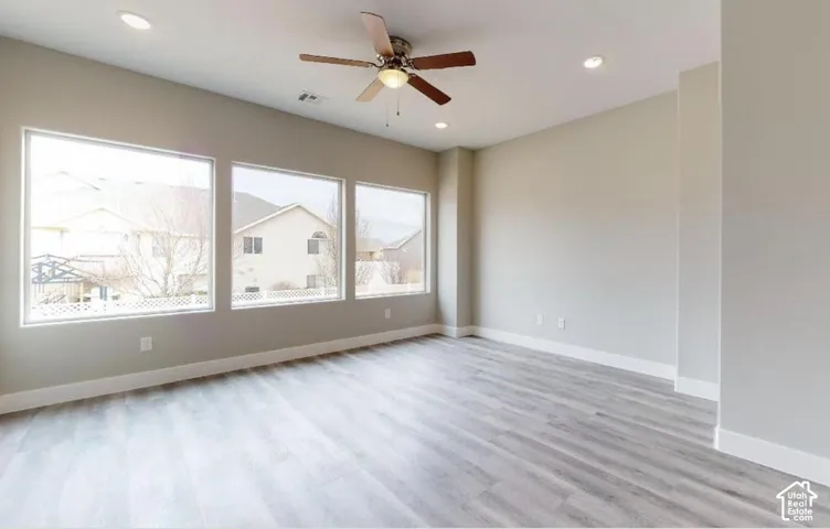 Neutral-toned interior featuring wood-finish flooring, recessed lighting, a ceiling fan, and three large windows