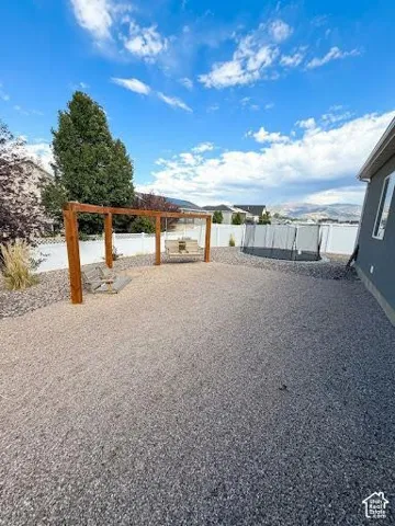 Low-maintenance gravel backyard featuring a wooden pergola, white vinyl fencing, and mountain horizon scenery