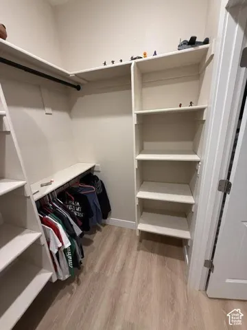 Walk-in closet featuring white built-in shelving, wooden closet rods, and wood-finish flooring