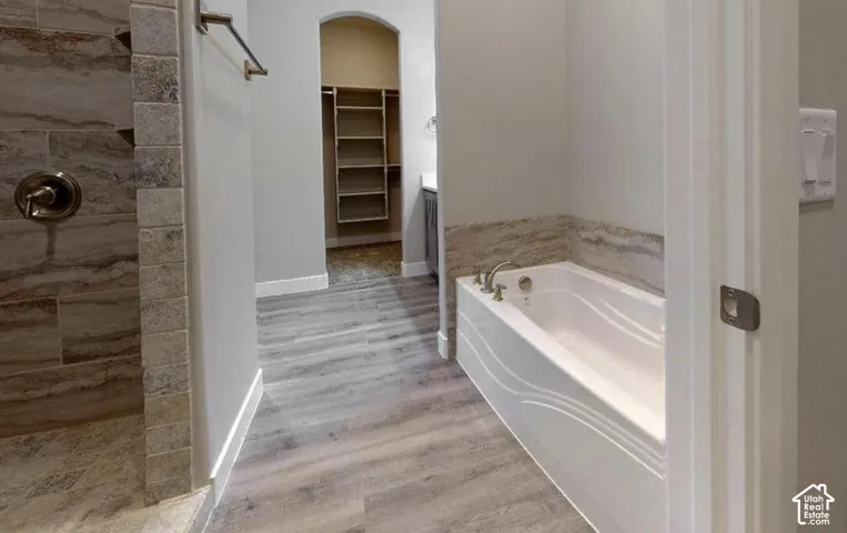 Bathroom featuring a walk-in shower with stone tile surround, soaking tub with tile backsplash, and wood-finish flooring