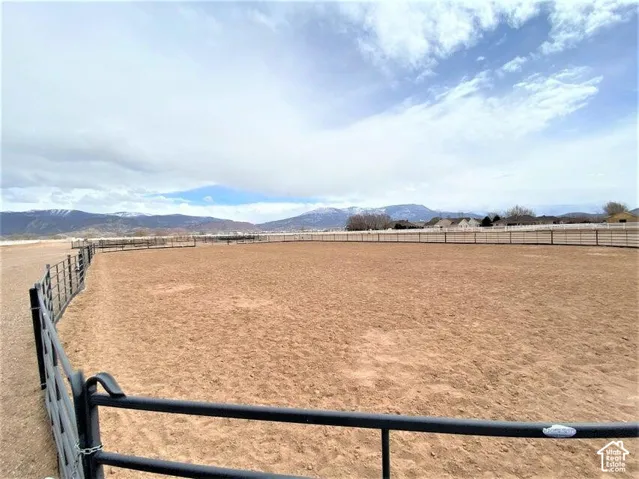 Outdoor arena featuring metal pipe fencing, packed earthen ground, and mountain backdrop