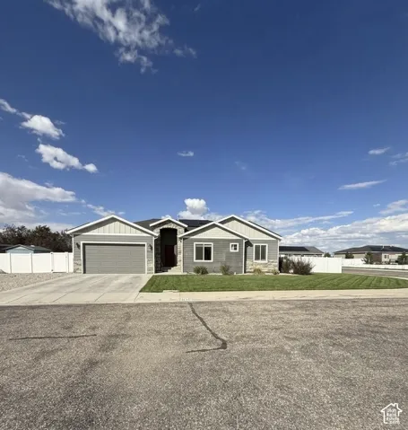Single-story residence featuring a gray lap-siding exterior with stone veneer accents, a concrete driveway, a dual-car garage, and a fenced perimeter