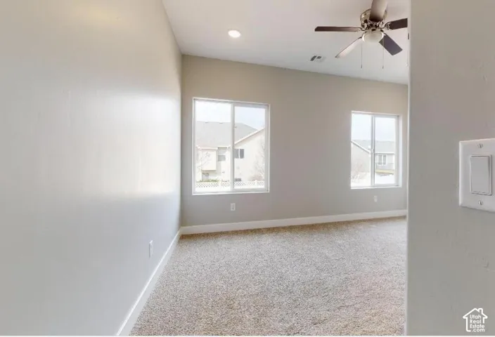 Neutral-toned interior featuring wall-to-wall carpeting, recessed lighting, dual sliding-sash windows, and a multi-blade ceiling fan