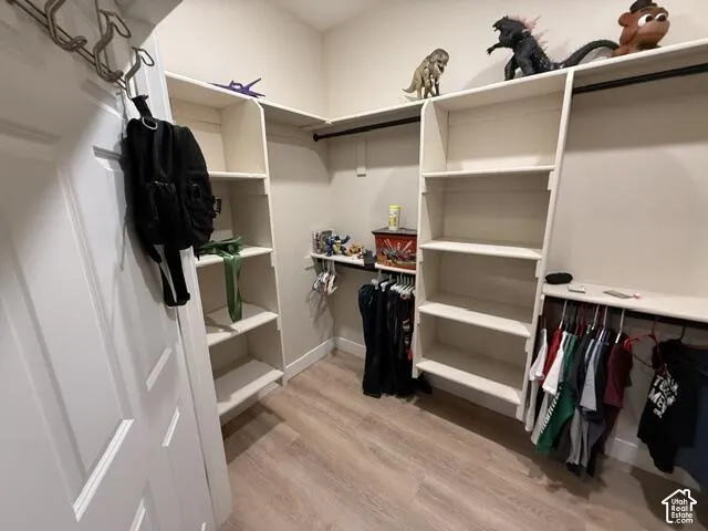 Walk-in closet featuring white built-in shelving, wooden rods, and wood-finish flooring
