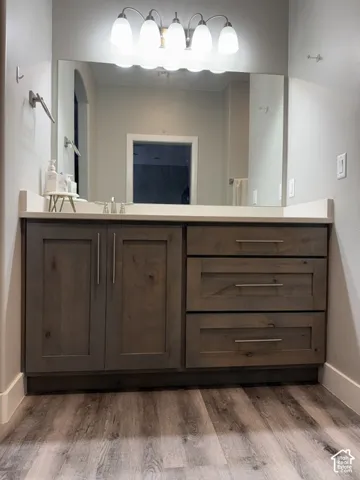 Bathroom vanity featuring wood-finish cabinetry, a solid-surface countertop, integrated rectangular sink, brushed-metal hardware, and a five-light fixture
