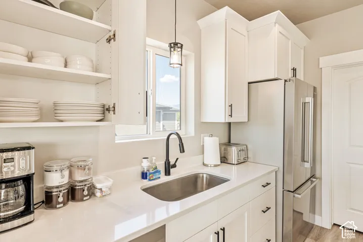 Kitchen featuring white shaker-style cabinetry with crown molding, quartz countertops, stainless steel undermount sink, matte black pull-down faucet, and a pendant light