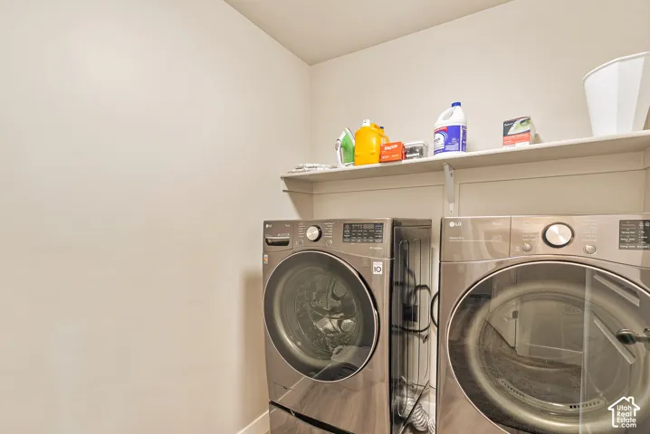 Laundry space featuring front-load metallic finish appliances and an elevated storage shelf
