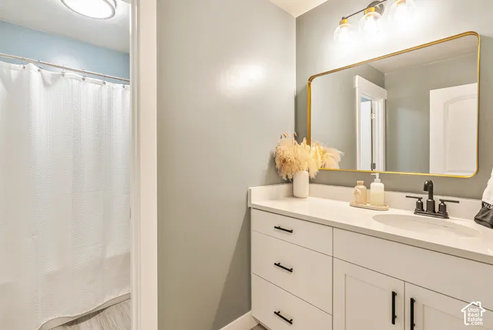 Bathroom featuring a white vanity with drawers, stone-finish countertop, undermount sink with matte black hardware, gold-tone framed mirror, and three-bulb vanity lighting