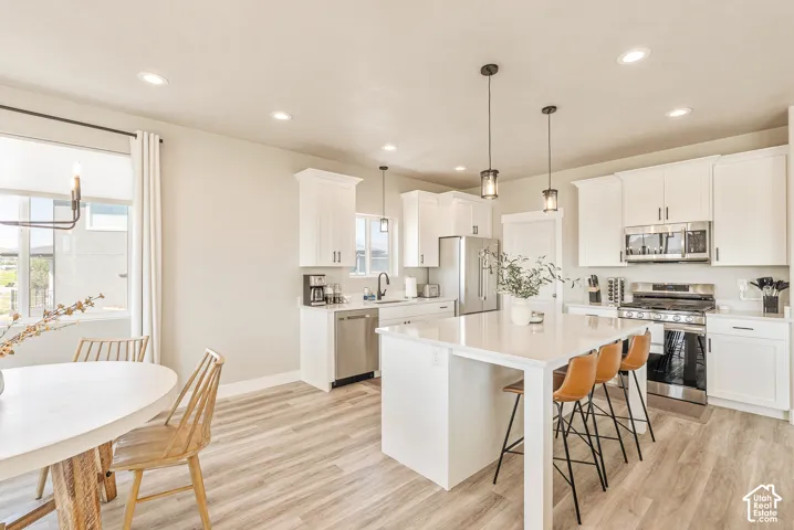 Kitchen featuring white shaker-style cabinetry, a central island with a solid surface countertop, stainless steel appliances, recessed ceiling lighting, and wood-finish flooring