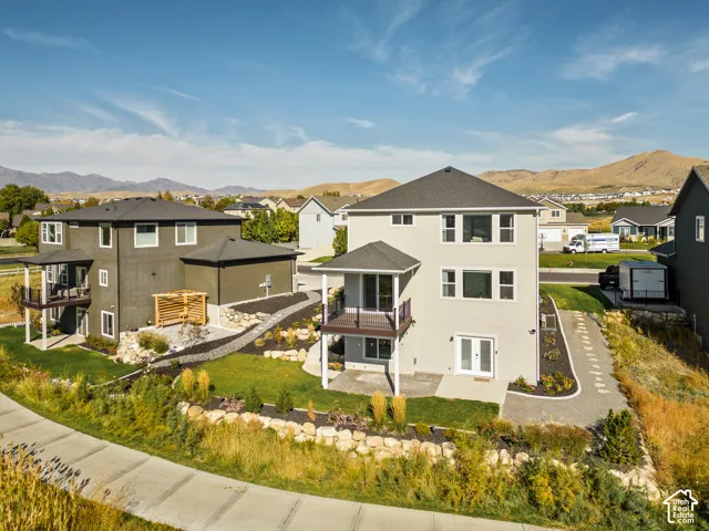 Two-story homes with stucco exteriors, shingle roofing, elevated railed balconies, and covered patio spaces, featuring landscaped grounds with stone retaining walls and mountain scenery