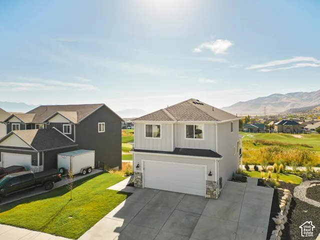 Two-story residence featuring a board-and-batten siding exterior, stone veneer accents, an attached two-car garage, and a concrete driveway, set against a mountain backdrop