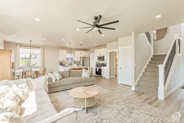 Open-concept interior featuring wood-finish flooring, recessed lighting, a modern ceiling fan, and a staircase with a white balustrade and dark metal spindles