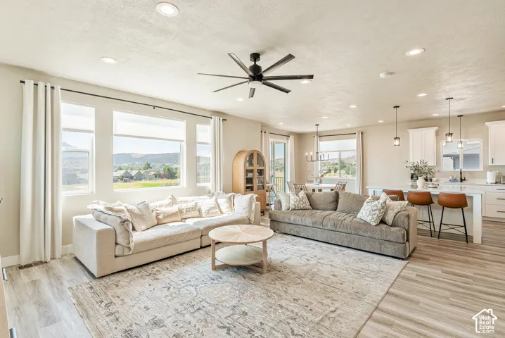 Open-concept interior featuring wood-finish flooring, recessed lighting, a modern ceiling fan, large windows with mountain scenery, and white cabinetry