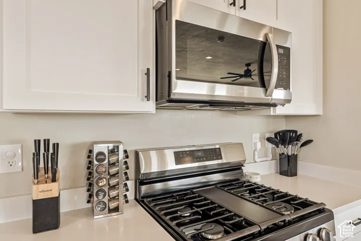 Shaker-style white cabinetry with matte black hardware, stainless steel over-the-range microwave, stainless steel gas range, and neutral solid-surface countertops