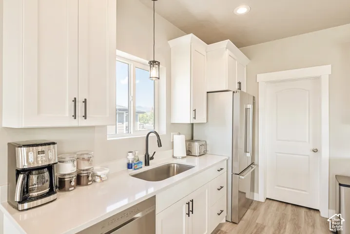 Kitchen featuring white cabinetry, solid-surface countertops, stainless steel appliances, a single-basin undermount sink with a gooseneck faucet, and wood-finish flooring