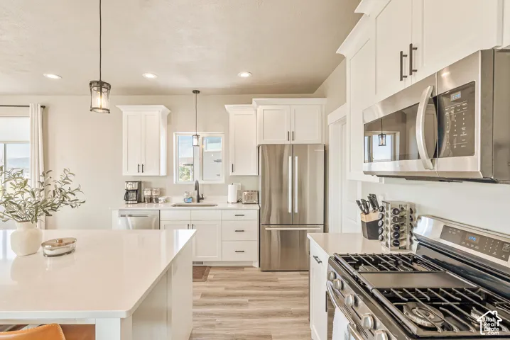 Kitchen featuring white shaker-style cabinetry, a quartz-topped island, stainless steel appliances, and wood-finish flooring