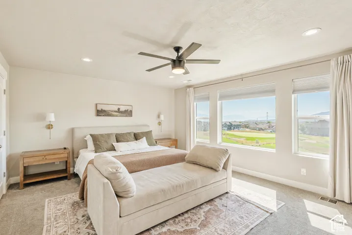 Room featuring neutral-toned carpeting, a multi-blade ceiling fan with integrated lighting, recessed ceiling lights, wall-mounted light fixtures, and triple-pane windows