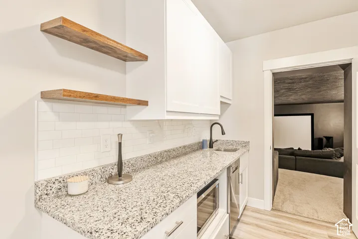 White shaker-style cabinetry, stone-finish countertops, subway tile backsplash, floating wood-finish shelving, and a matte black gooseneck faucet