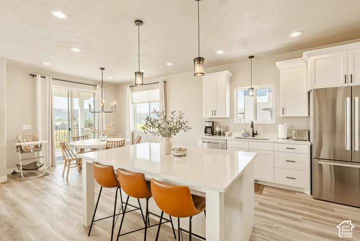Kitchen featuring white shaker-style cabinetry, quartz countertops, a central island with bar seating, stainless steel appliances, and wood-finish flooring