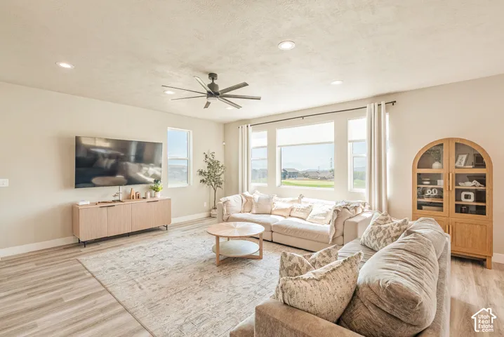 Living area featuring wood-finish flooring, recessed lighting, a multi-blade ceiling fan, and large windows providing natural light
