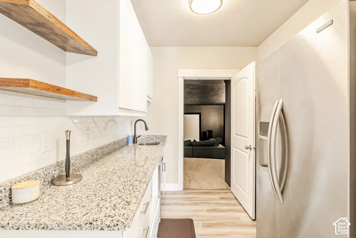 Kitchenette featuring white cabinetry, stone-finish countertops, subway tile backsplash, wood-finish open shelving, and a stainless steel refrigerator