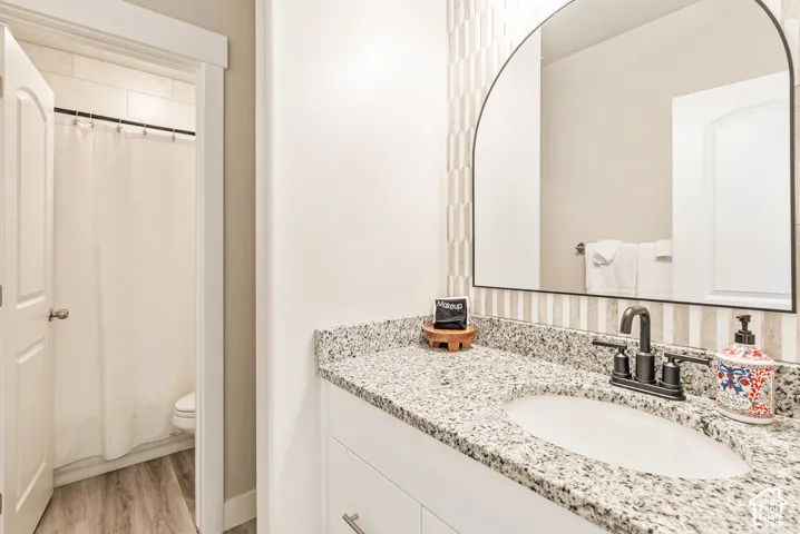 Bathroom vanity featuring a stone countertop, an integrated oval sink, a matte black faucet, an arched wall mirror, and vertically patterned tile backsplash