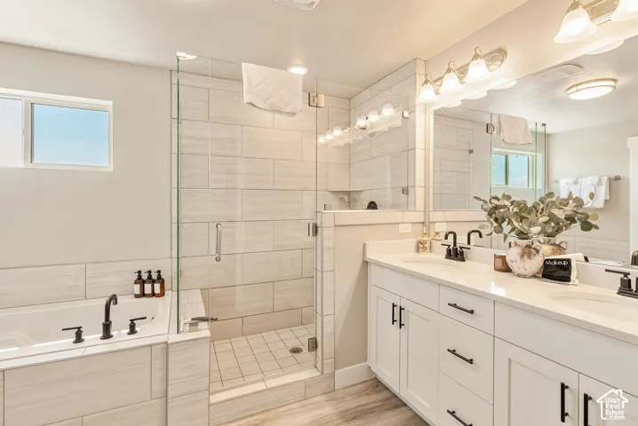 Bathroom featuring a dual-sink vanity with matte black fixtures, a walk-in glass shower enclosure, a soaking tub with a tiled surround, and expansive wall-to-wall mirror