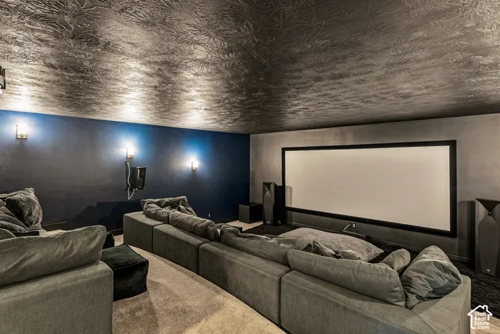 Media room featuring a recessed screen, custom textured ceiling, dark-toned wall finish, and wall-mounted sconce lighting