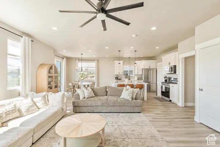 Open-concept interior featuring wood-finish flooring, recessed lighting, a modern ceiling fan, and white kitchen cabinetry with stainless steel appliances