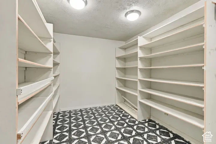 Storage area featuring extensive built-in shelving and patterned vinyl flooring, illuminated by dual ceiling-mounted light fixtures
