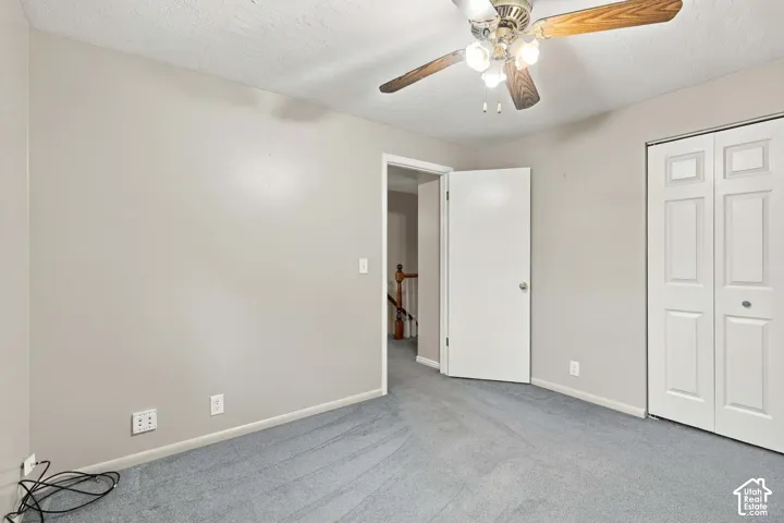 Neutral-toned interior room featuring wall-to-wall carpeting, a ceiling fan with integrated lighting, and a double-door closet