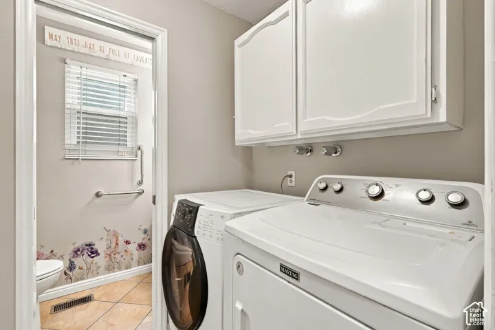 Laundry area featuring white wall-mounted upper cabinetry and laundry hookups, with a tiled floor visible in the threshold