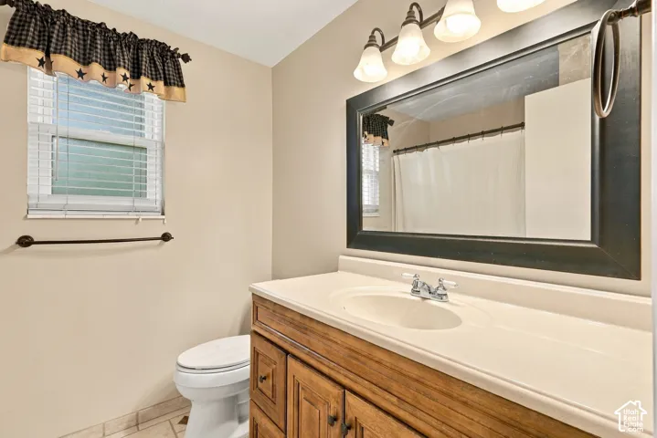 Bathroom featuring a wood-finish vanity with an integrated basin, a large rectangular mirror with a dark frame, a multi-bulb light fixture, and tile flooring